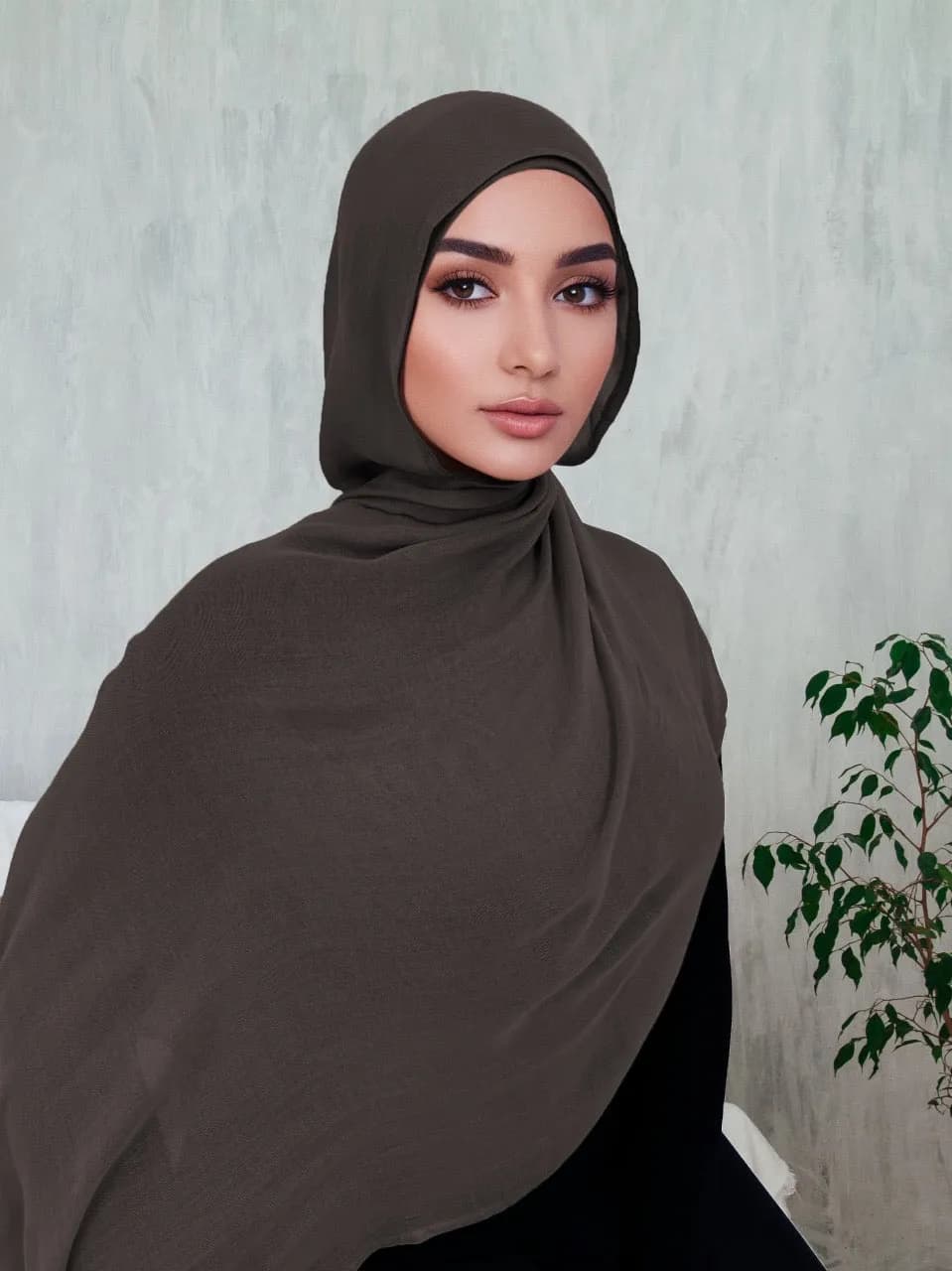 Woman wearing an olive hijab against grey wall